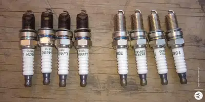 Cuatro bujías gastadas junto a cuatro bujías nuevas